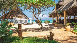 A beachside restaurant with a thatched roof, surrounded by palm trees and potted plants. - Tanzanite Beach Resort (Nungwi)