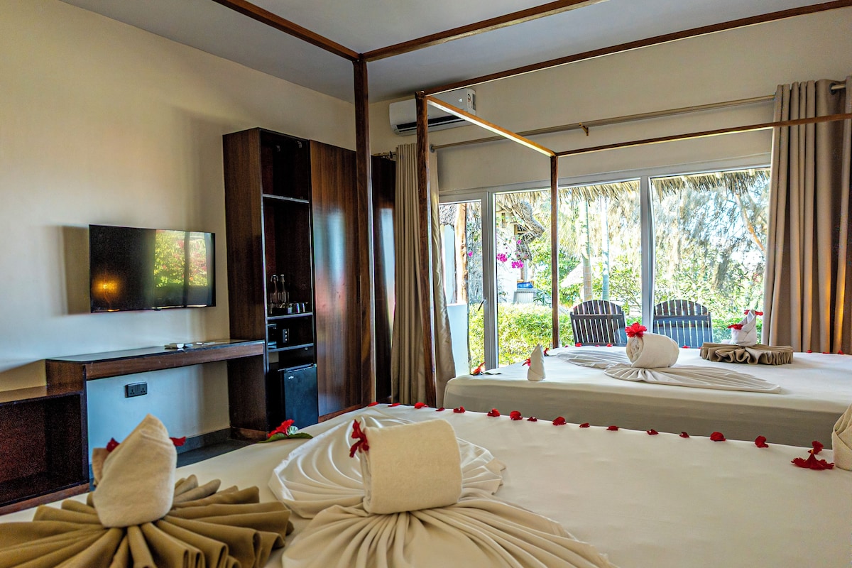 A hotel room with a bed, a TV, a minibar, and a window with a view of greenery.