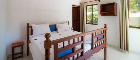 A bedroom with a wooden bed, a small bedside table, a window with curtains, and an air conditioning unit on the wall.