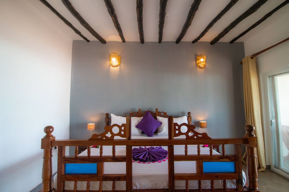 A bedroom with a wooden bed frame, two wall-mounted lamps, and a window with curtains.