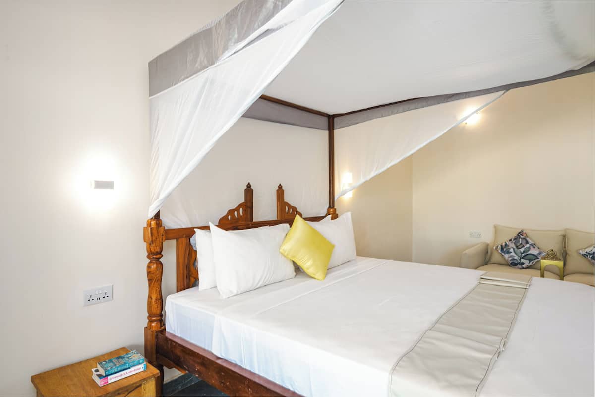 A four-poster bed with white linens and a yellow pillow, a bedside table with books, and a nightstand with a lamp.
