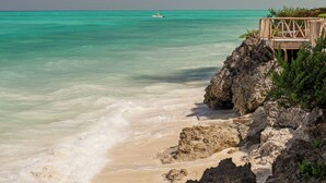 A beach with clear turquoise water, a wooden pier, and rocky terrain. - Tanzanite Beach Resort (Nungwi)