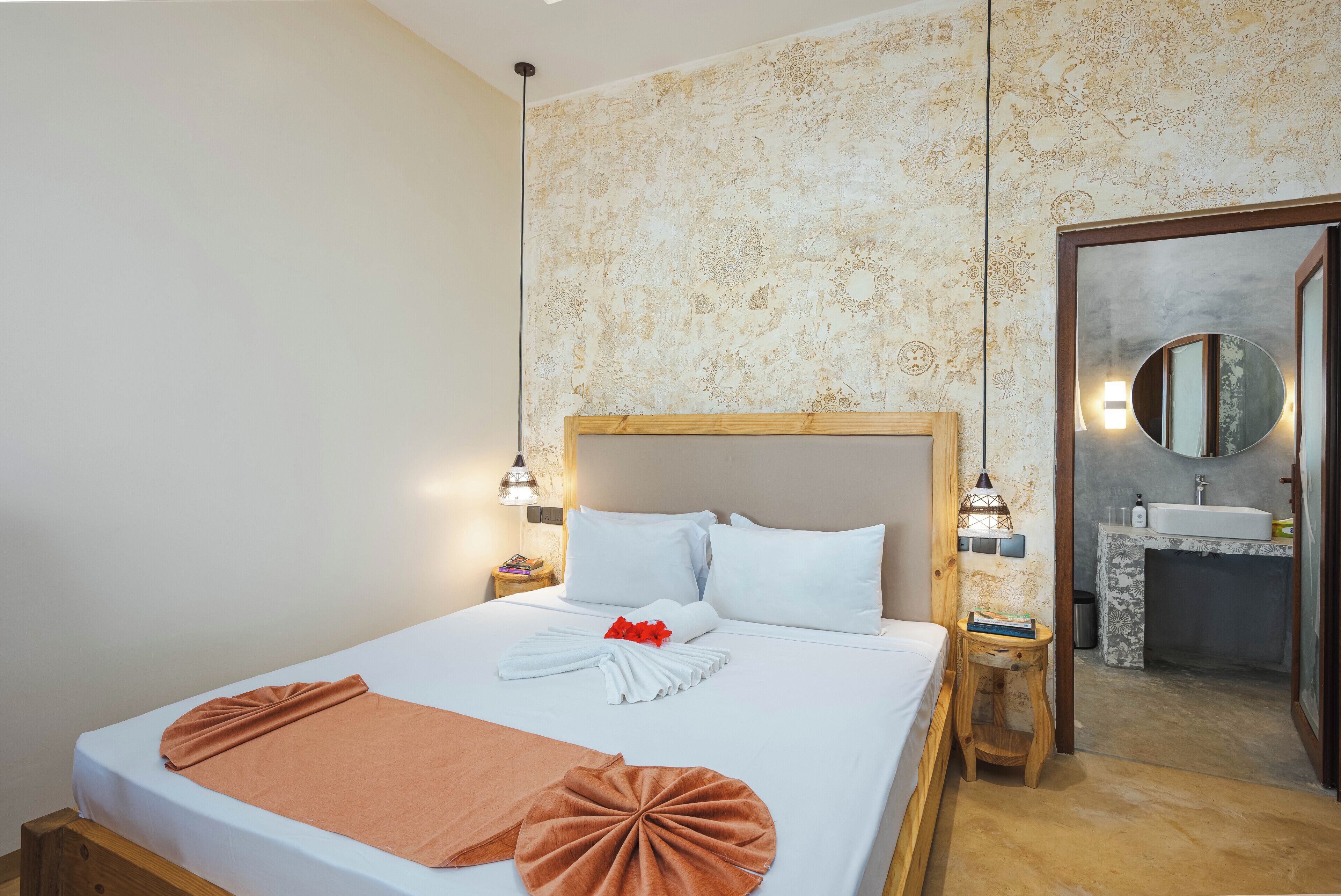 A hotel room with a large bed, a wooden headboard, a bedside table with a lamp, and a bathroom visible through an open door.