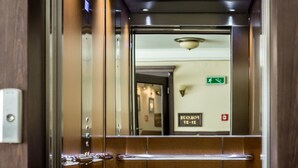 An elevator interior with metallic walls, a reflective floor, and a visible emergency exit sign. - Hotel Krzyski (Tarnow)
