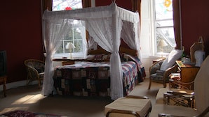 A bedroom with a four-poster bed, a sitting area with chairs, and a window with curtains. - The Manor Country House Hotel (Dumfries)