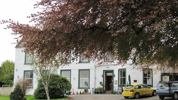 A white building with green trim, a yellow taxi parked in front, and a tree with red leaves. - The Manor Country House Hotel (Dumfries)