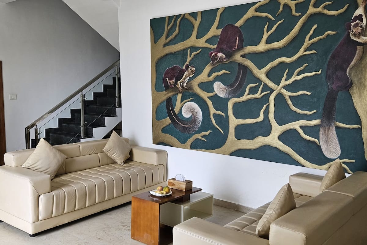 A living room with a beige sofa, a coffee table, and a painting of a tree with squirrels.