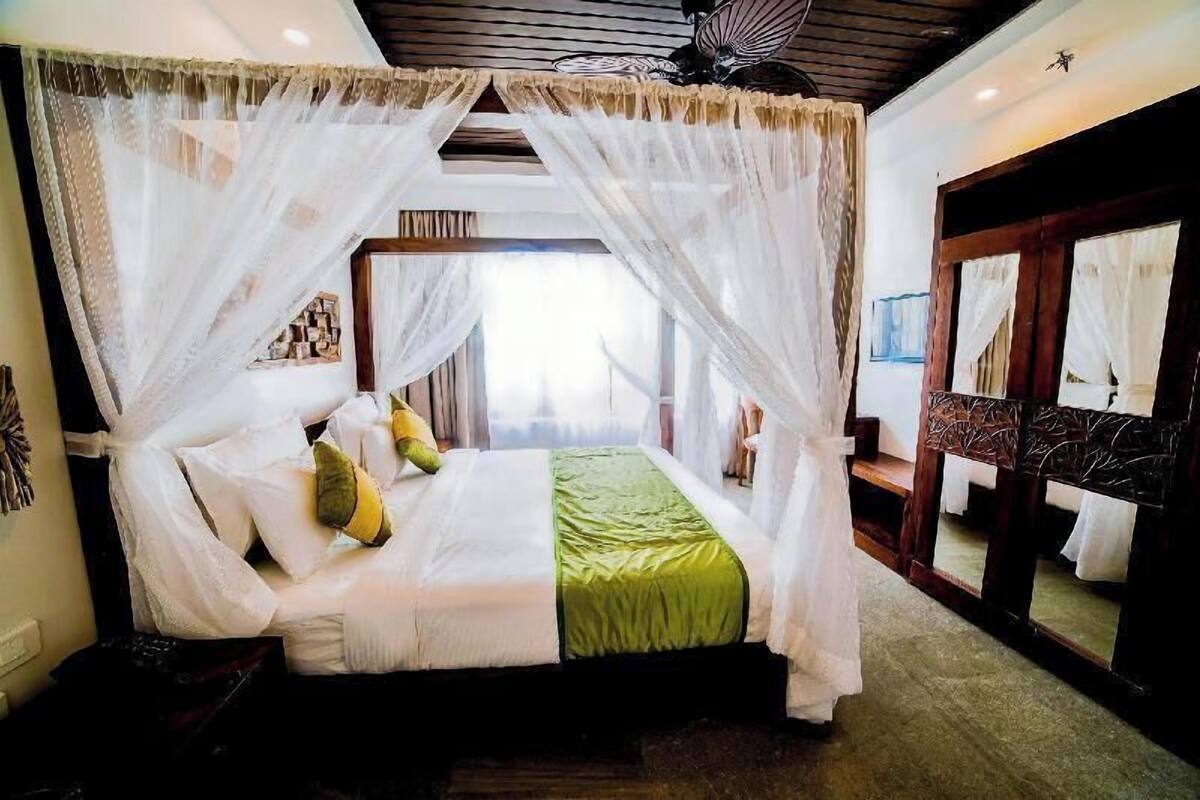 A four-poster canopy bed with a green bedspread, a wooden headboard, and a large mirror with a decorative frame.