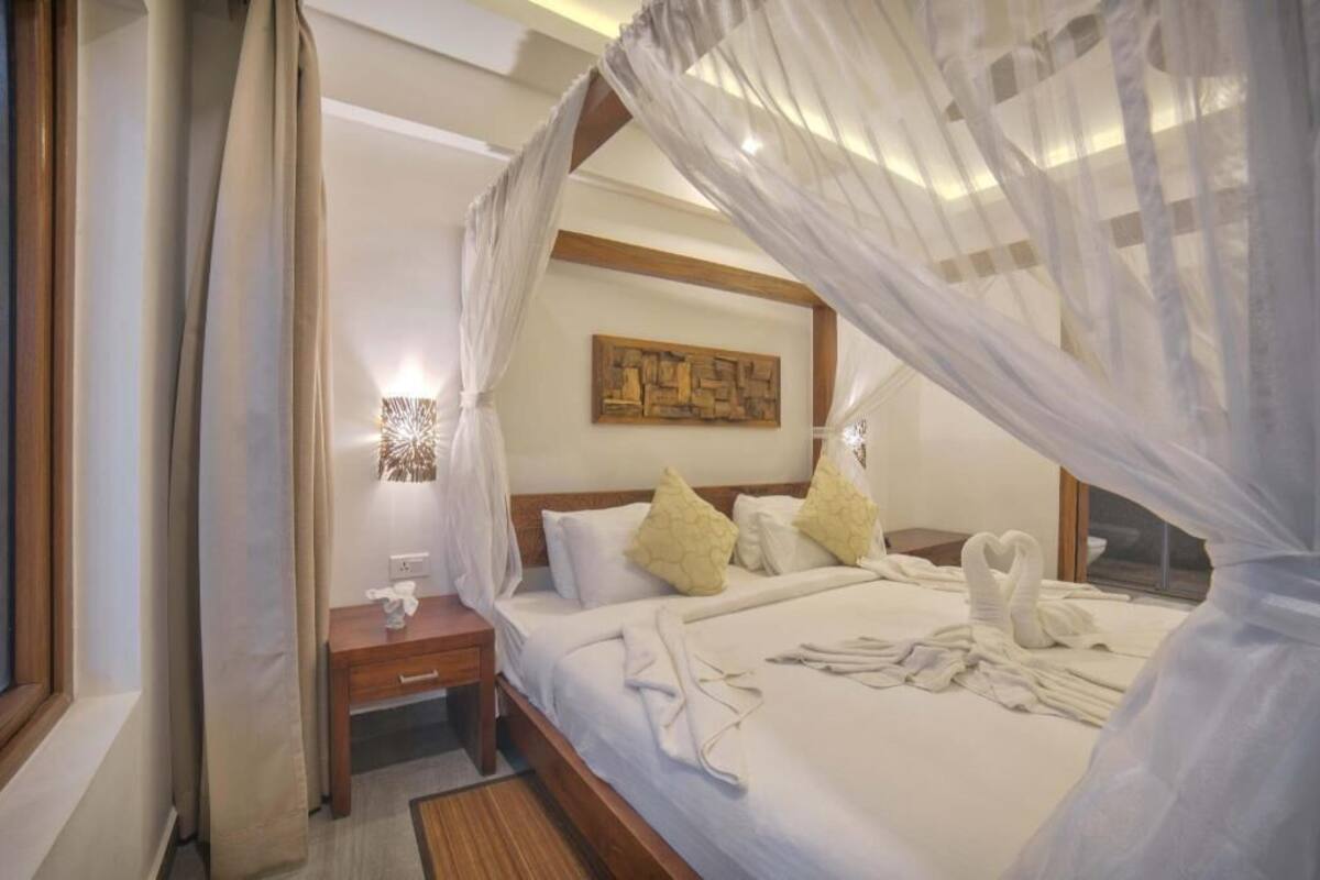 A hotel room with a bed, a nightstand, a bedside table, a wall-mounted artwork, and a window with curtains.