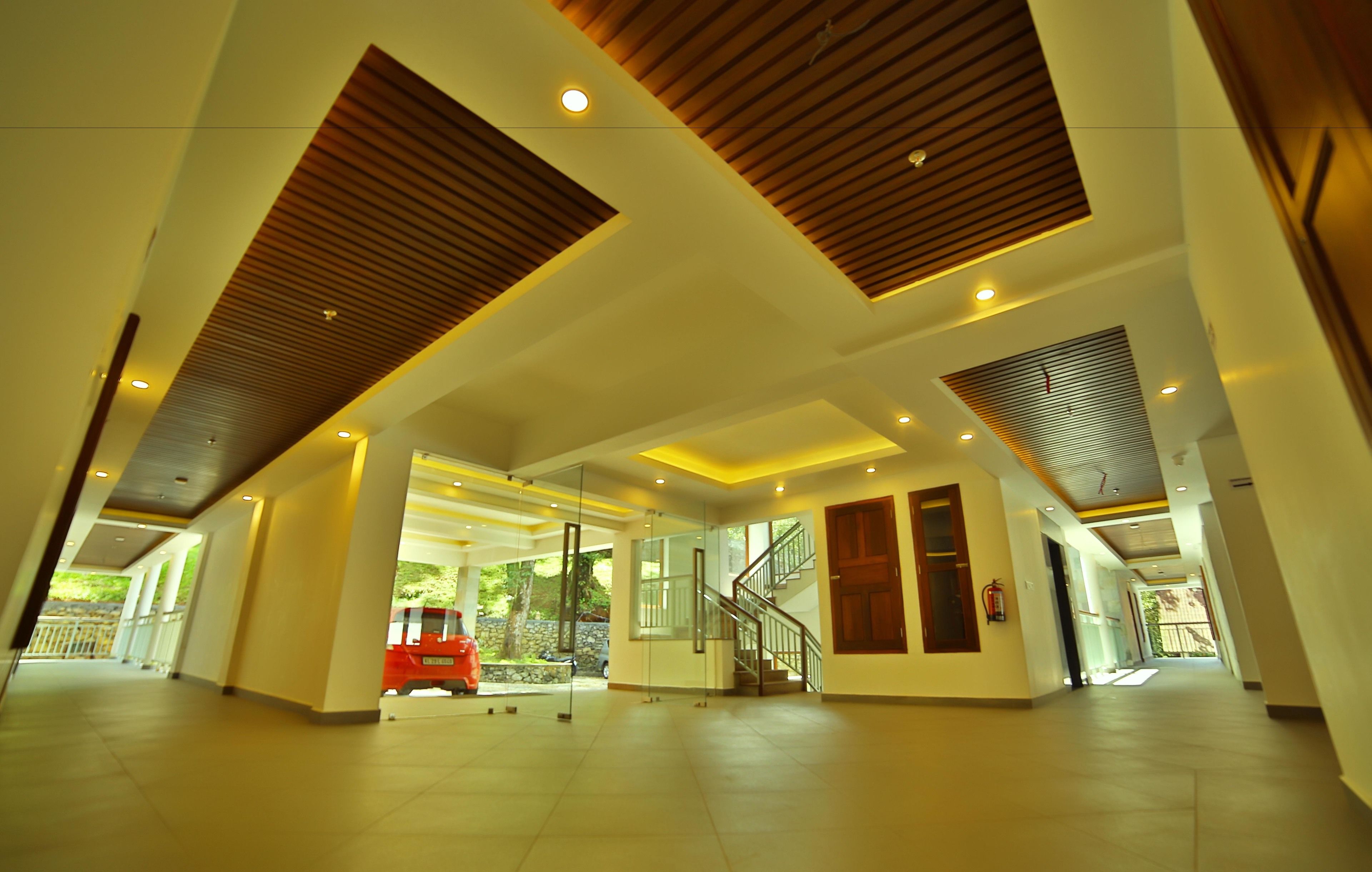 A spacious lobby with a modern design, featuring a central staircase, glass doors leading outside, and a red vehicle parked outside.