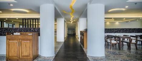 A hotel lobby with a central hallway flanked by wooden cabinets and a dining area with chairs.