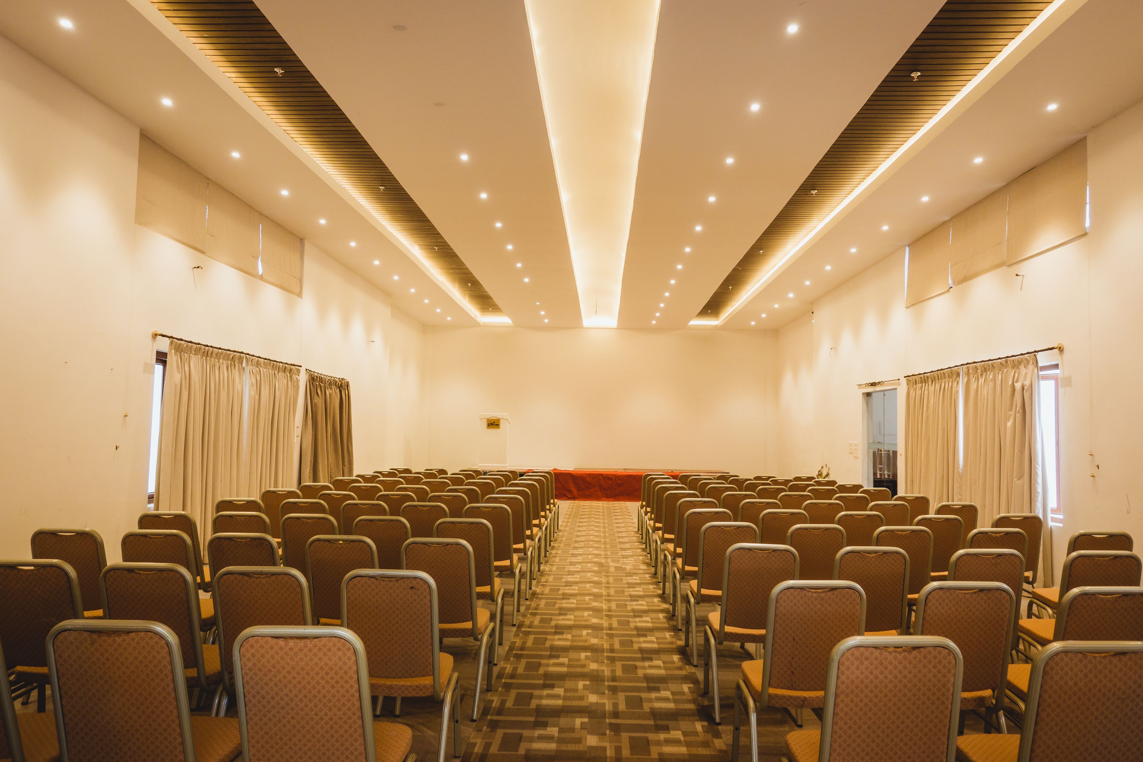 A conference room with rows of chairs, a podium, and curtains on the windows.