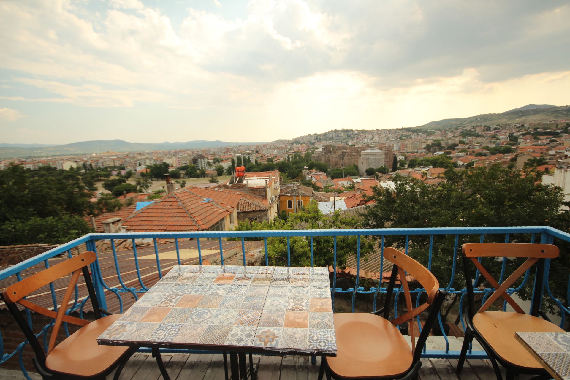 A terrace with a table and chairs, overlooking a cityscape with buildings and hills.
