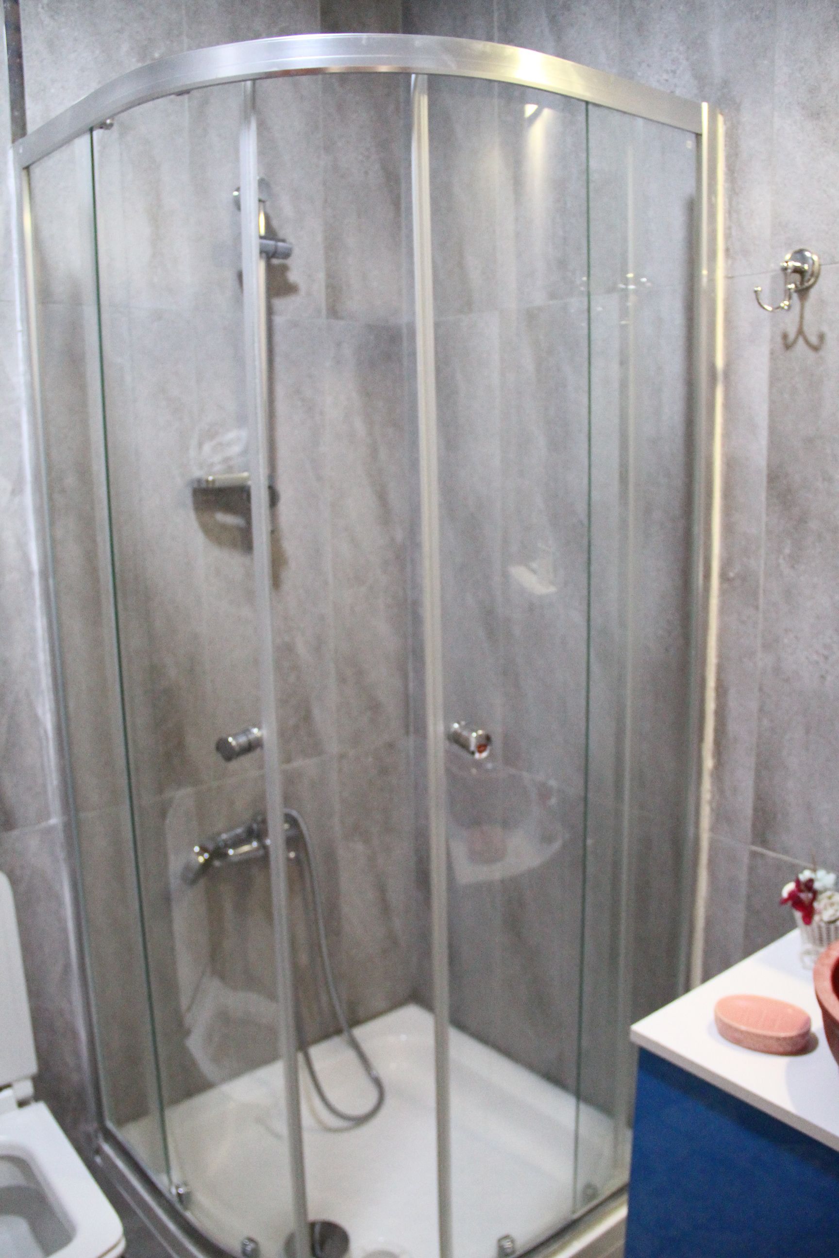 A glass-enclosed shower stall with a white sink and a blue countertop to the right.