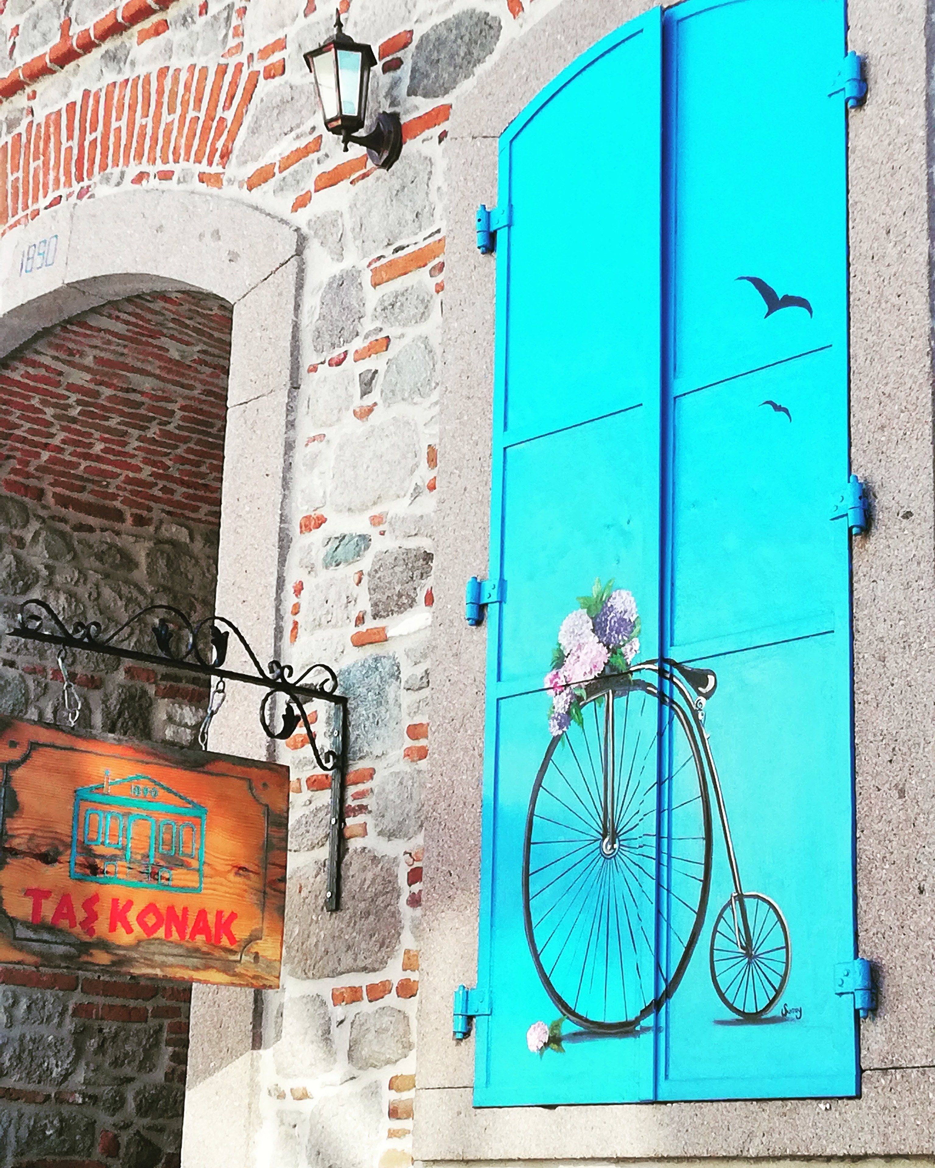 Un edificio con una puerta azul turquesa, un letrero que dice "TAS KONAK" y un muro de piedra con un arco de ladrillo.