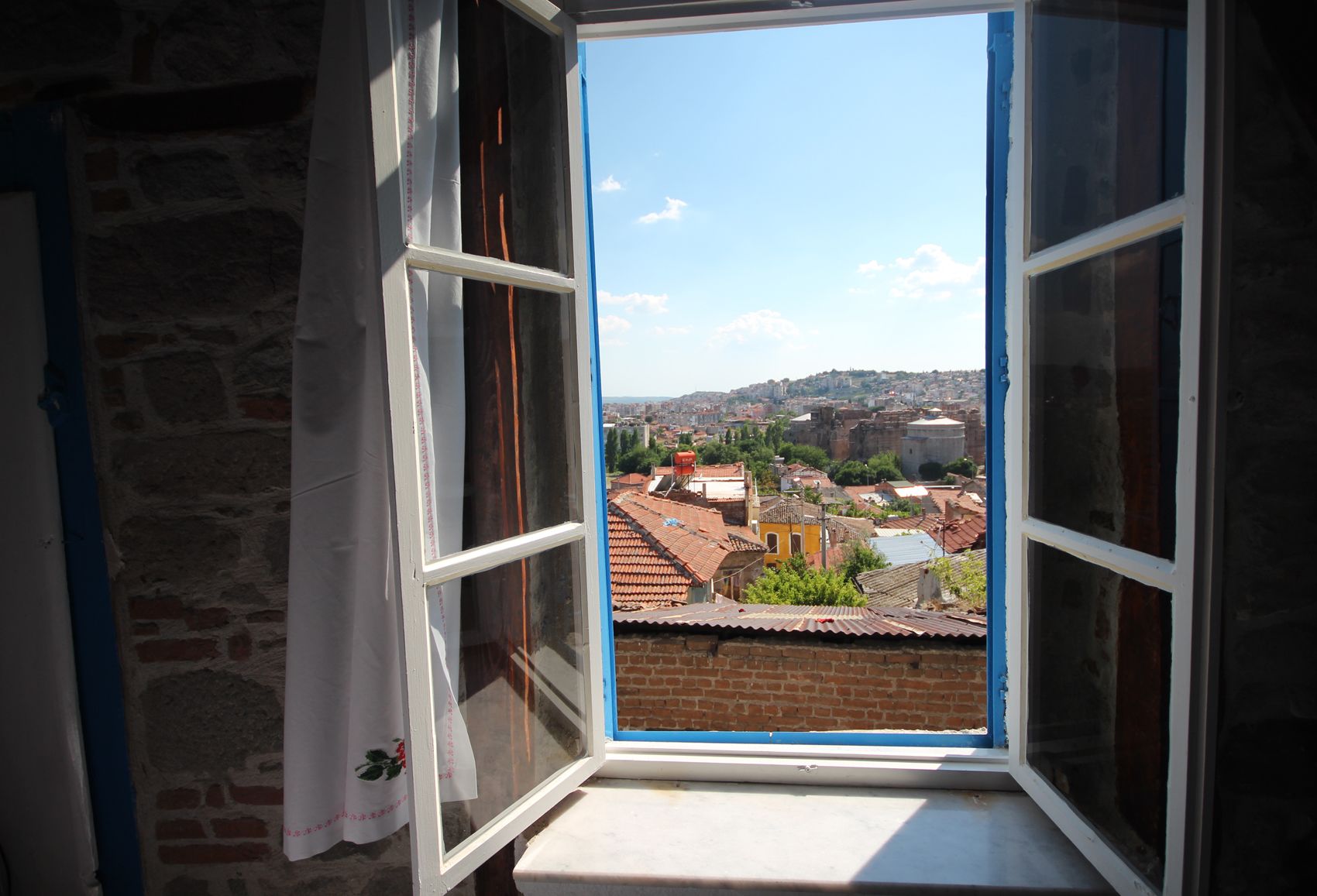 Una ventana con vista a un paisaje urbano, que incluye edificios y una colina distante.