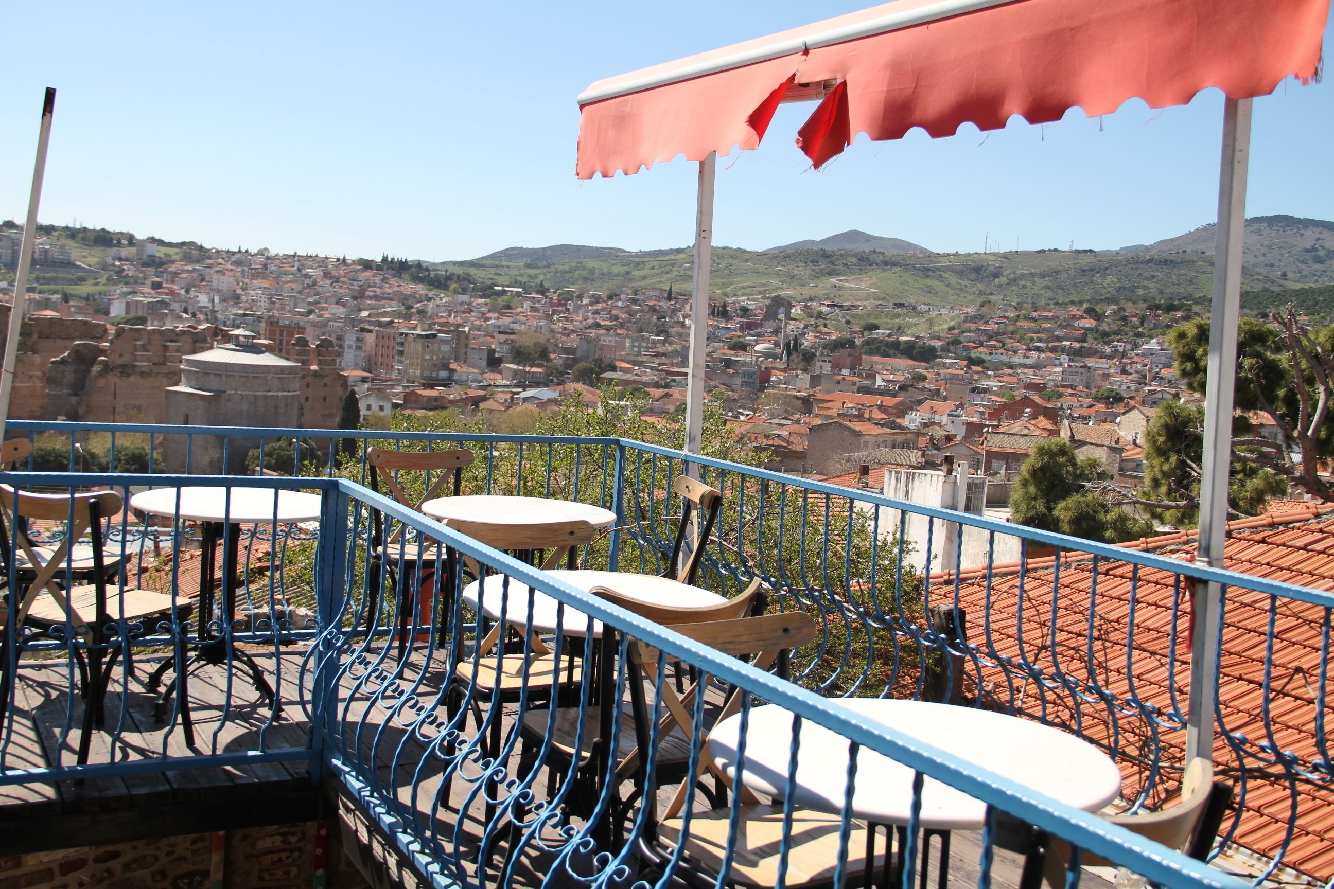 A terrace with tables and chairs, overlooking a cityscape with buildings and hills.