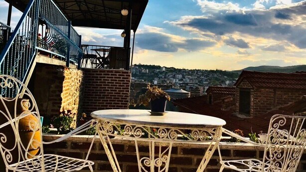 A rooftop terrace with a round table and white metal chairs, overlooking a cityscape. - Bergama Tas Konak (Bergama)