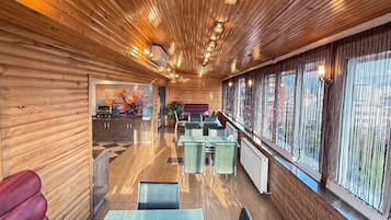 A restaurant with wooden paneling, green tables, and chairs, and a view through large windows.