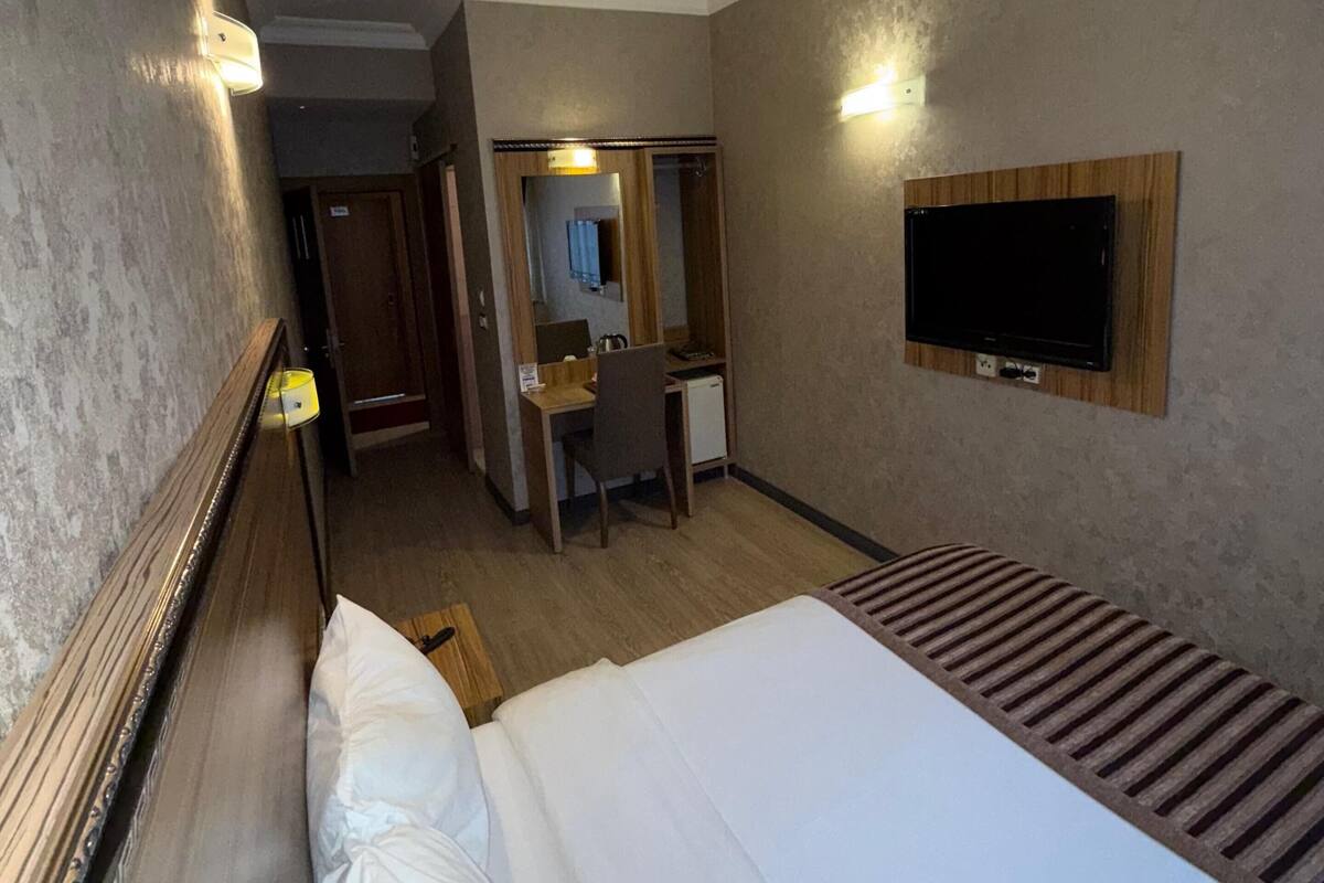 A hotel room with a bed, a desk, a chair, a TV, and a wardrobe.