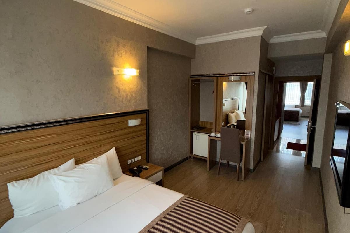 A hotel room with a large bed, a desk, a mirror, and a wardrobe.