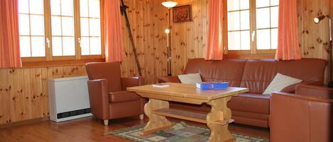 A living room with a wooden floor, a brown leather sofa, a wooden coffee table, and a radiator.