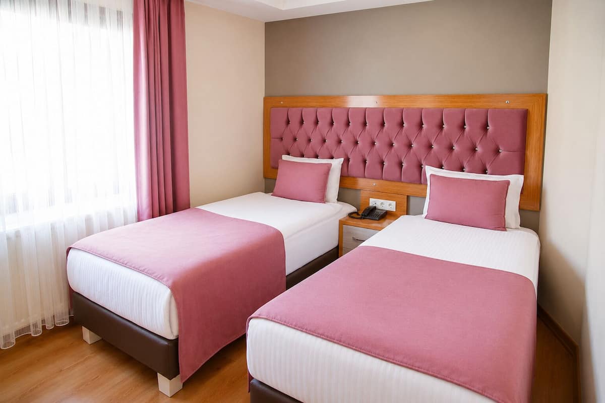 A hotel room with two beds, a wooden headboard, a nightstand with a phone, and a window with curtains.