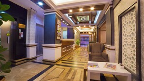 A hotel lobby with a reception desk, seating area, and a patterned floor.