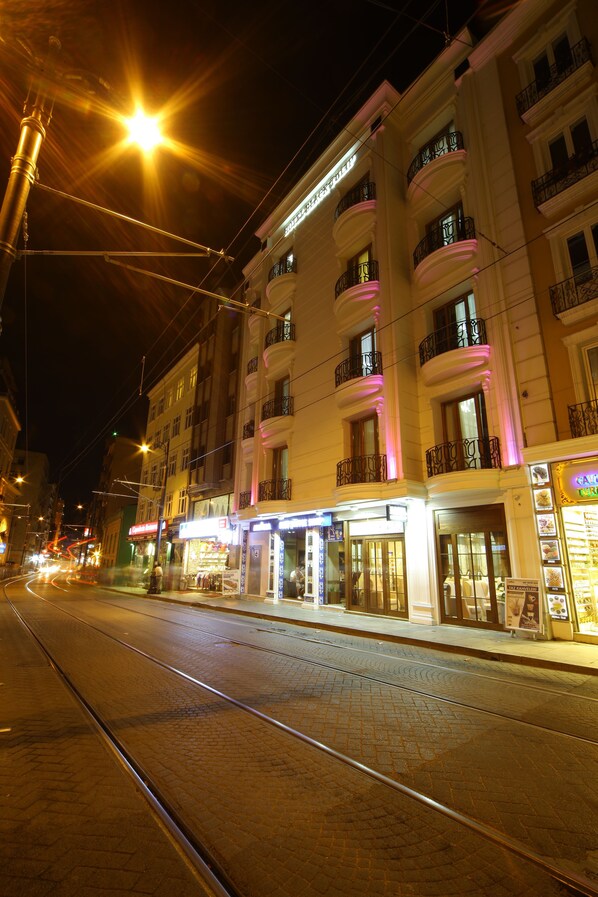 A street with tram tracks, illuminated buildings with balconies, and storefronts. - Weingart Black Pearl (Istanbul)
