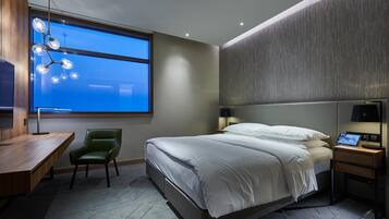 Ein modernes Hotelzimmer mit einem großen Bett, einem Schreibtisch, einem Stuhl und Blick auf den Himmel durch ein großes Fenster.
