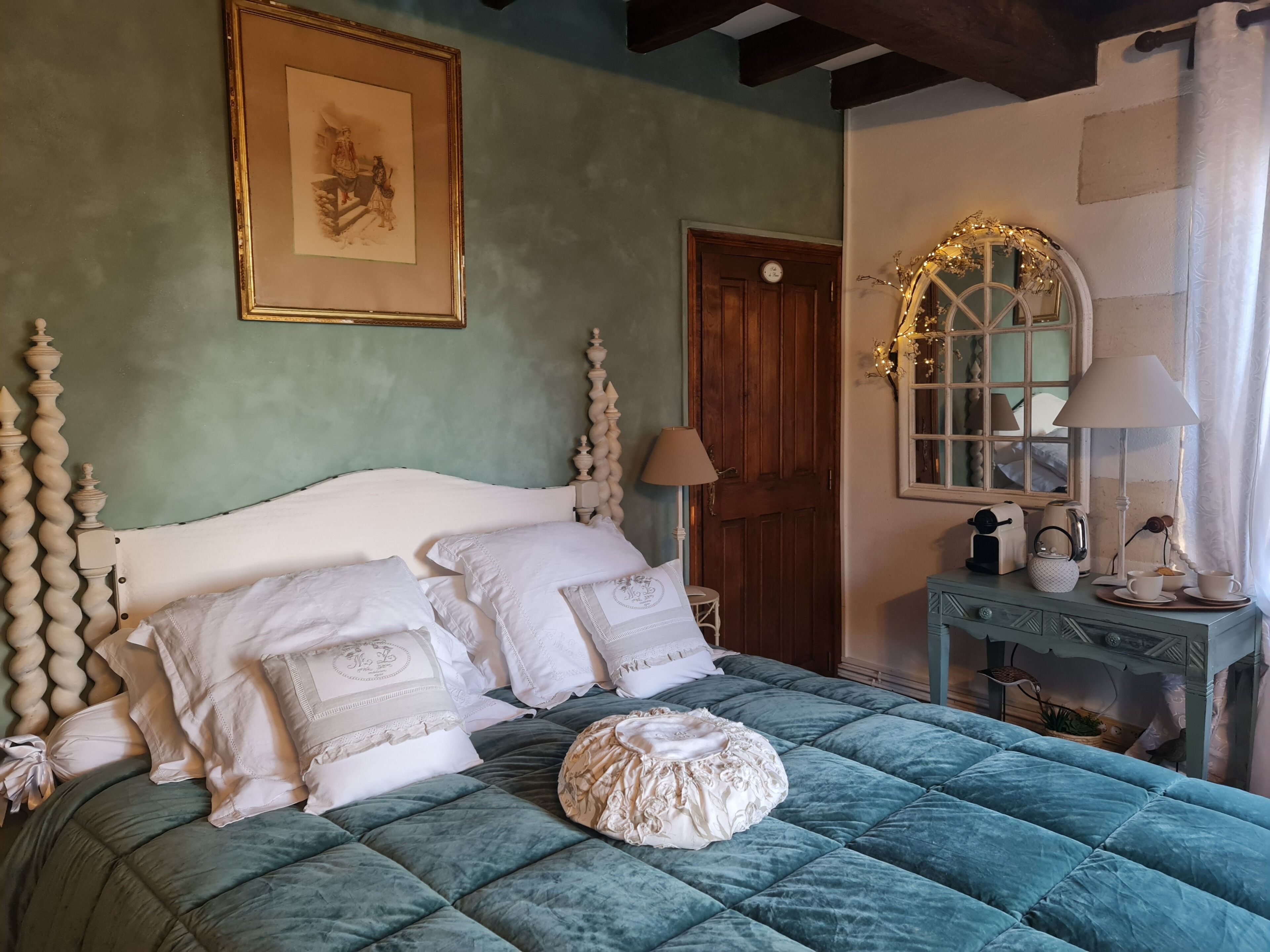A bed with a quilted green cover, white pillows, and a decorative headboard.
