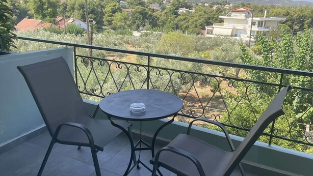 A balcony with a round table and two chairs, overlooking a residential area with houses and greenery. - Hotel Paradise (Oropos)