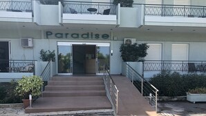 A building with a sign reading "Paradise" at the entrance, featuring a staircase leading up to the door, metal railings, and potted plants around the entrance. - Hotel Paradise (Oropos)