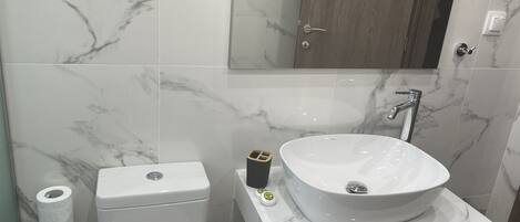 A bathroom with a toilet, a sink with a marble countertop, and a mirror above the sink.