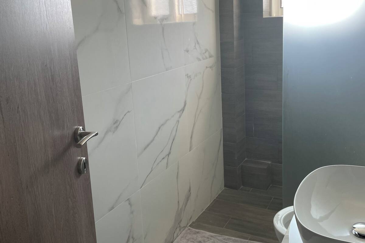 A bathroom with marble walls, a wooden door, a white sink, and a small window.