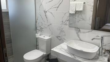 Et moderne badeværelse med toilet, bidet og vask med marmorbeklædt bagvæg.