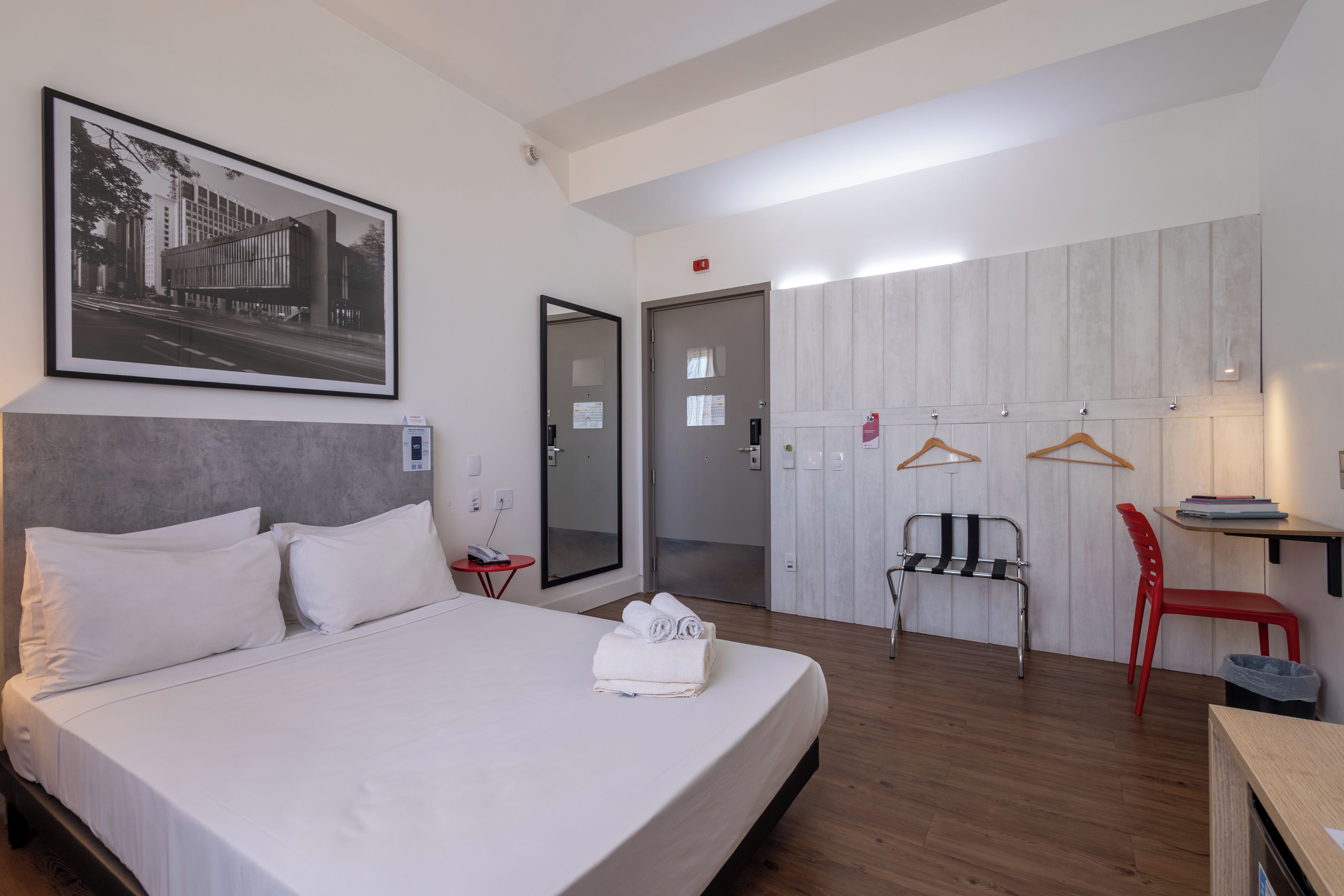 A hotel room with a bed, a desk, a chair, a wardrobe, and a door.