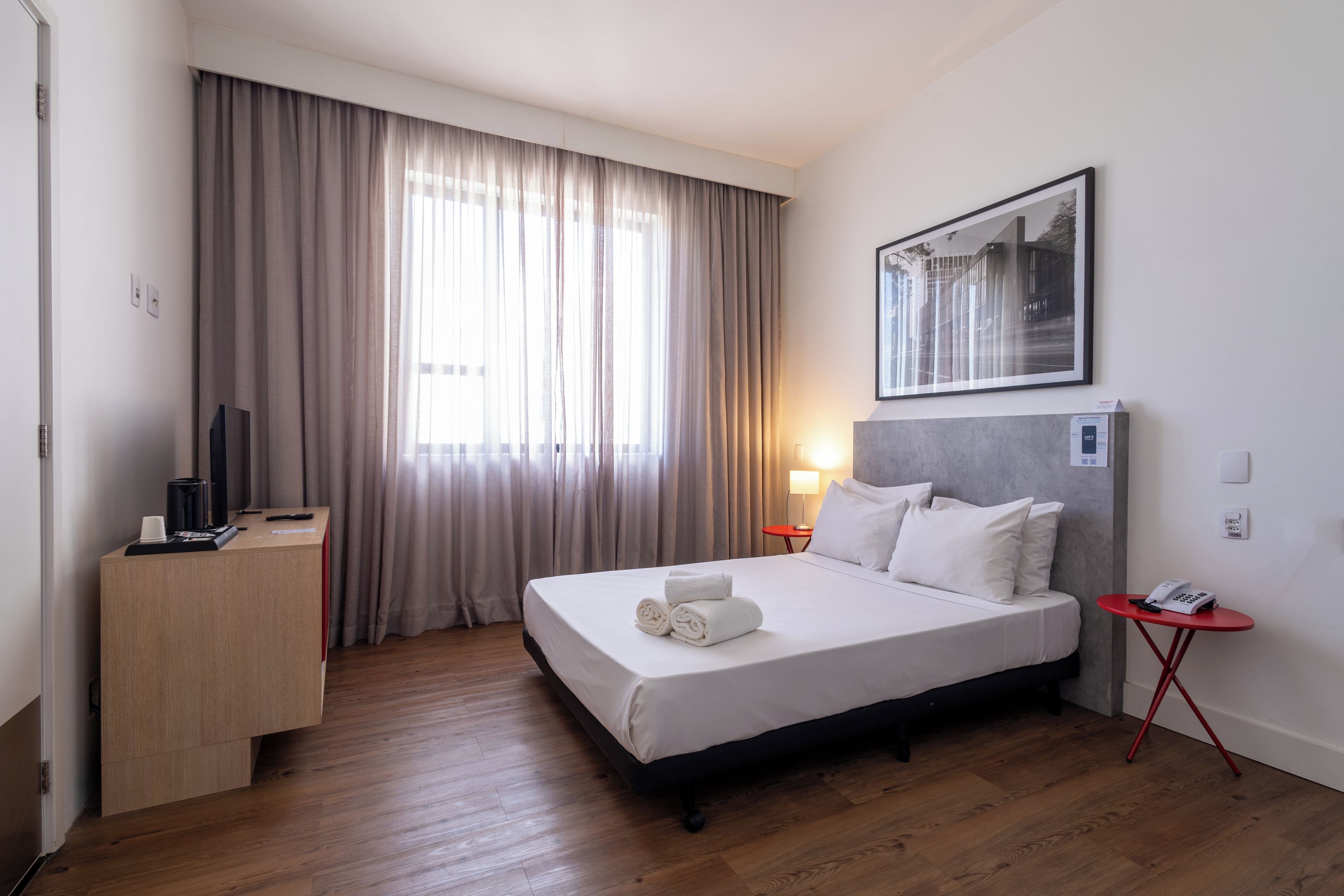 Una habitación de hotel con cama, escritorio, silla, lámpara y un cuadro en la pared.