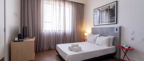 Una habitación de hotel con cama, escritorio, silla, lámpara y un cuadro en la pared.