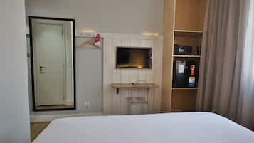 A hotel room with a bed, a TV mounted on the wall, a wardrobe, and a small desk with a chair.