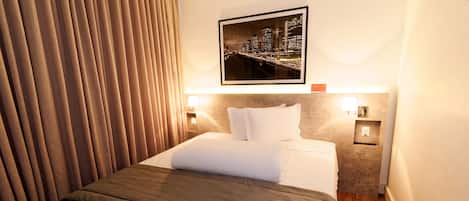 A hotel room with a neatly made bed, a cityscape picture on the wall, and a wooden floor.