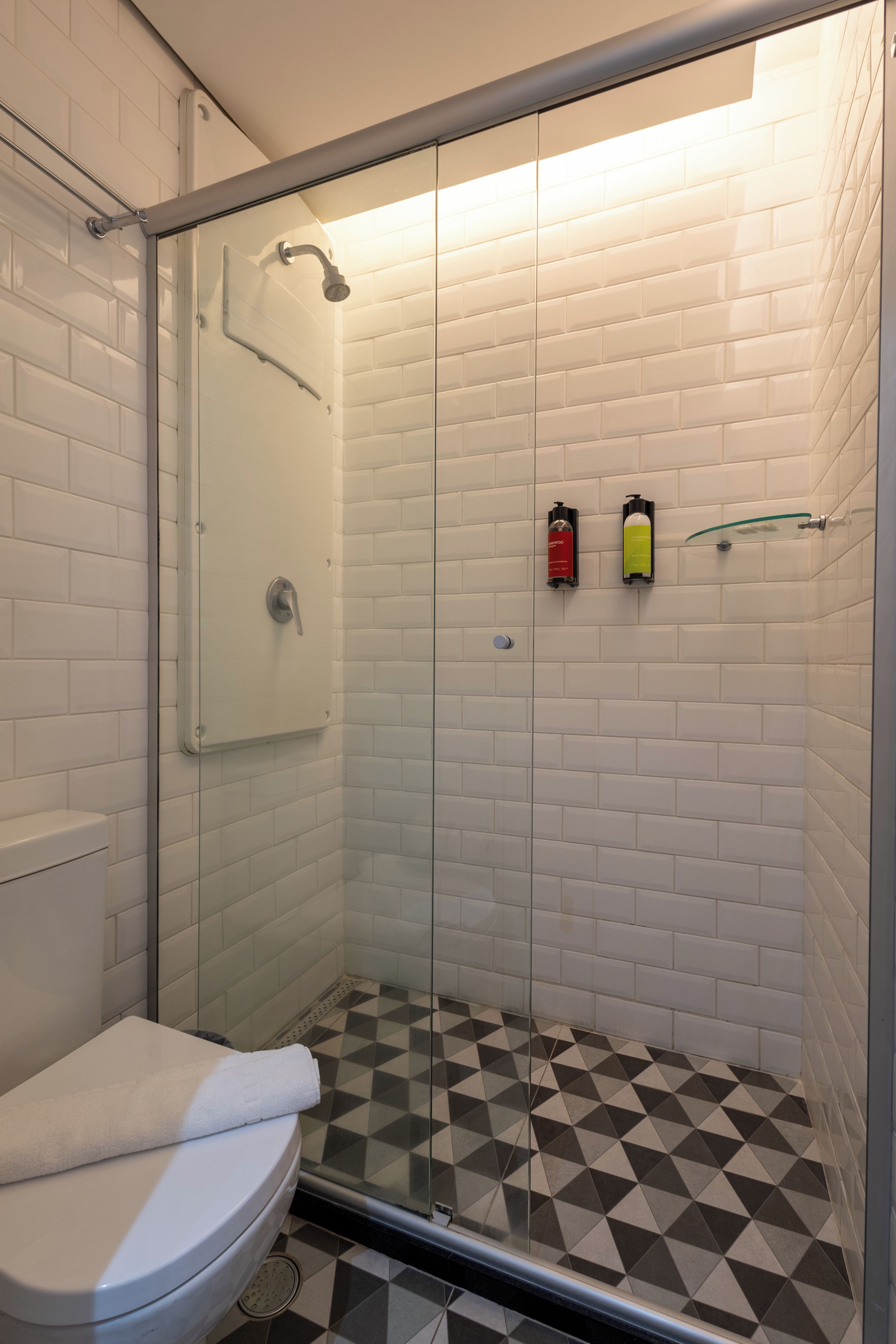 Una ducha con puerta de vidrio, un inodoro blanco y un piso con estampado de cuadros.