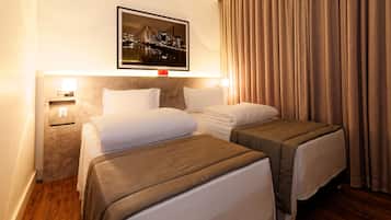 Habitación de hotel con dos camas, vistas a la ciudad, una mesita de noche con lámpara y una ventana con cortinas.