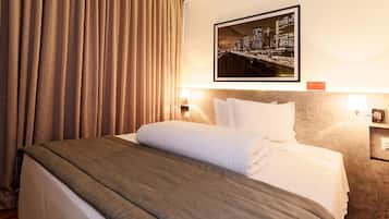 A neatly made bed with a grey bedspread and white pillows, a framed cityscape picture on the wall, and a lamp on the nightstand.