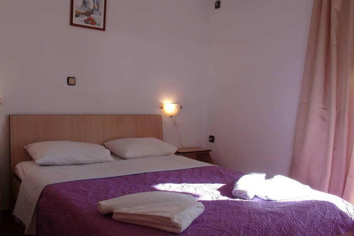 Una cama bien hecha con un edredón púrpura, dos lámparas de noche y un cuadro en la pared.