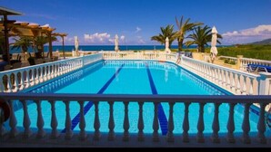 Una piscina con barandilla blanca, palmeras y cielo azul despejado.
