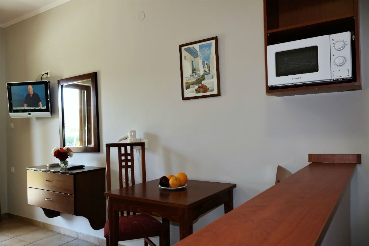 A room with a wooden dining table, a TV mounted on the wall, a microwave above the table, a mirror, and a framed picture on the wall.