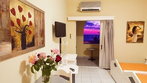 Un cuarto de hotel con una cama, un escritorio, una silla, un televisor, un cuadro y vistas al atardecer.