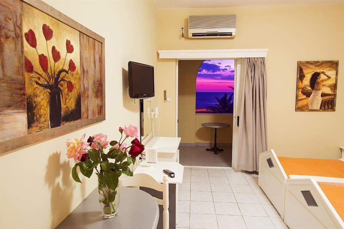 Un cuarto de hotel con una cama, un escritorio, una silla, un televisor, un cuadro y vistas al atardecer.
