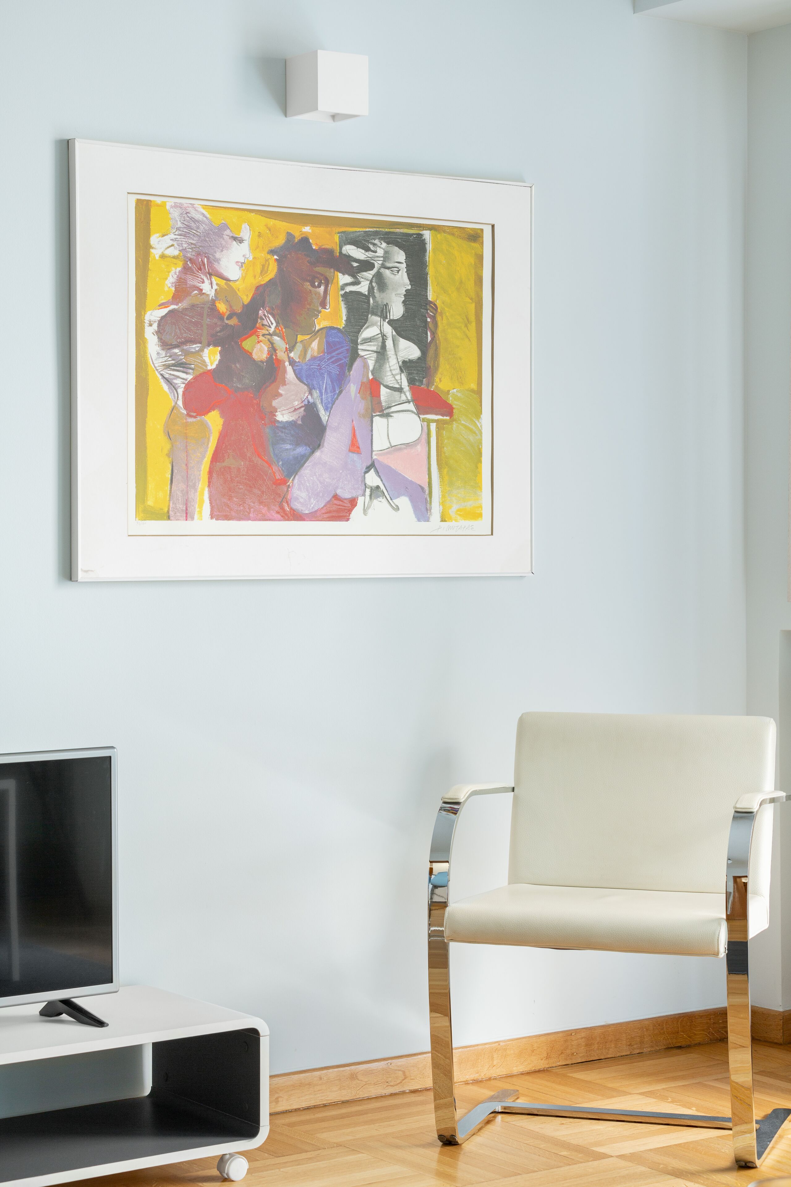 A room with a framed abstract painting, a white chair, and a TV stand.